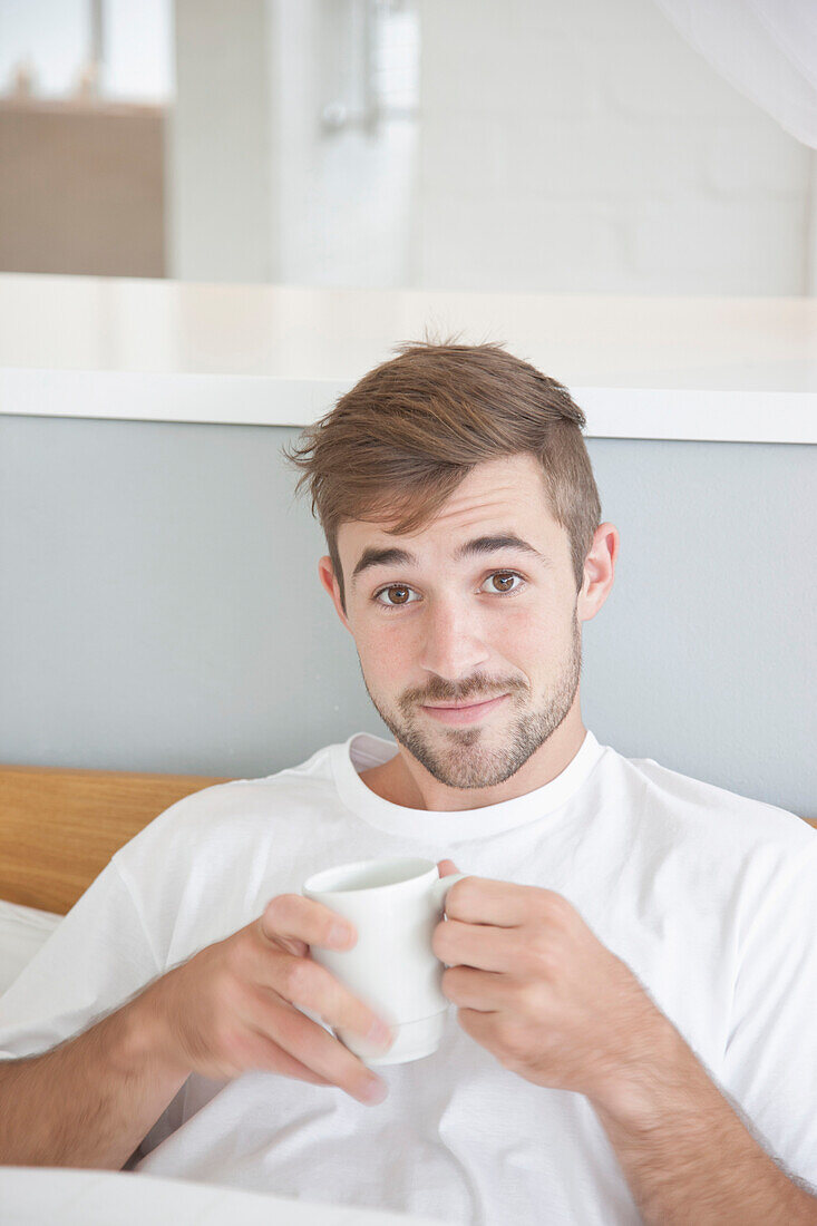 Mann sitzt im Bett und hält Tasse