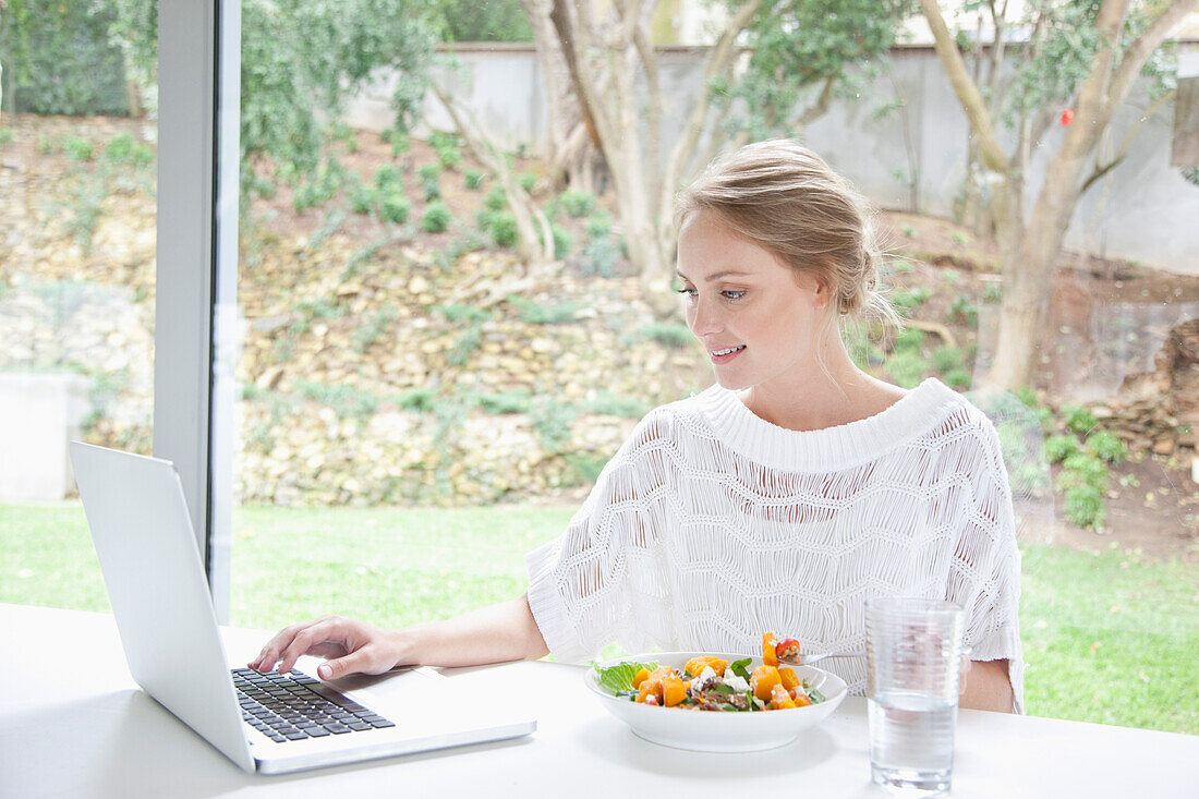 Frau isst Salat, während sie einen Laptop-Computer benutzt