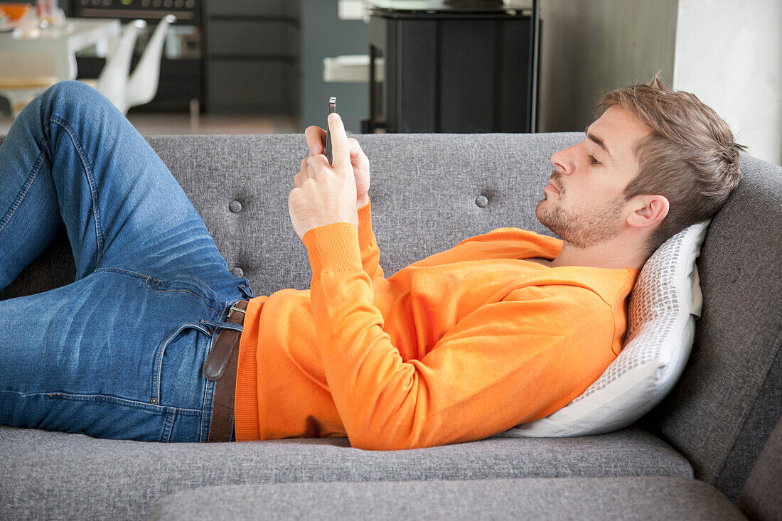 Mann auf Sofa liegend mit Smartphone