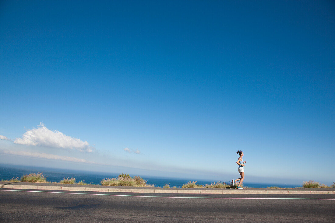 Woman Running along Asphalt Road by Ocean