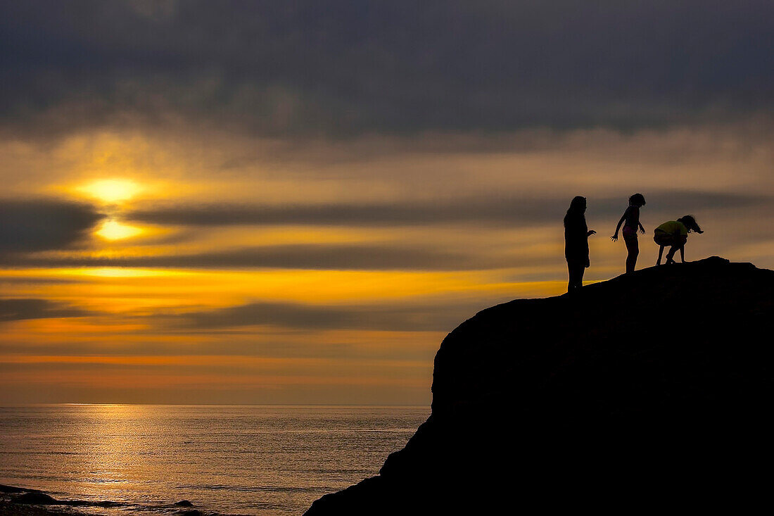 Silhouette von drei Teenager-Mädchen auf einer Klippe am Meer bei Sonnenuntergang