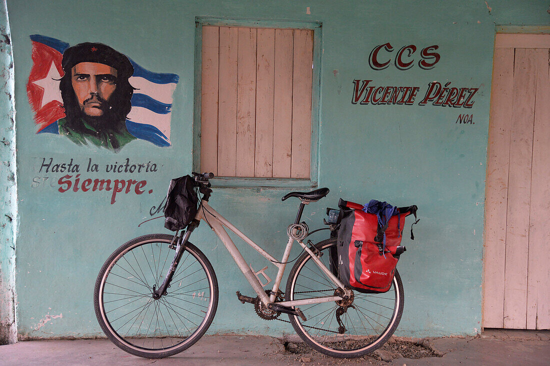 Kuba,ein Fahrrad ist gegen eine pastellblaue Wand geparkt, an der das Porträt von Che Guevara gemalt ist