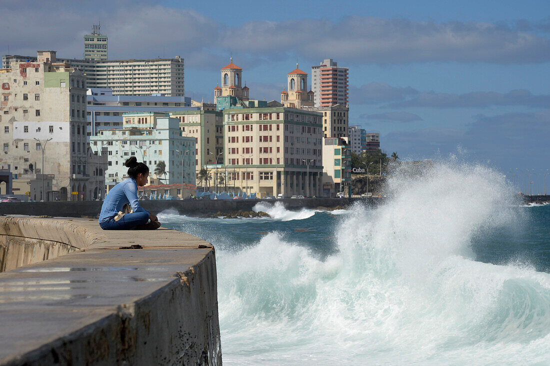 Cuba,La Havana,a young woman is sitting on the parapet in front of the ocean