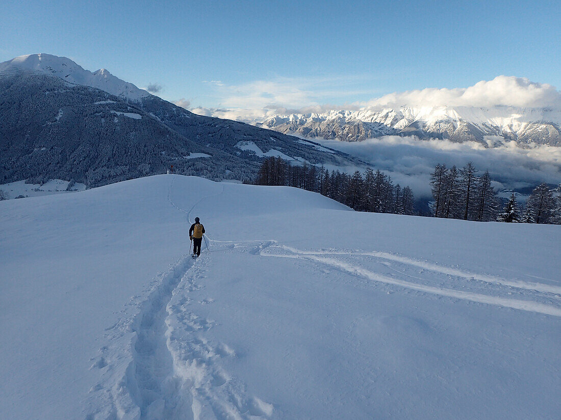 Austria,Tyrol,a man carrying a yellow backpack is hiking in the fresh snow in front of the Stubai Alps