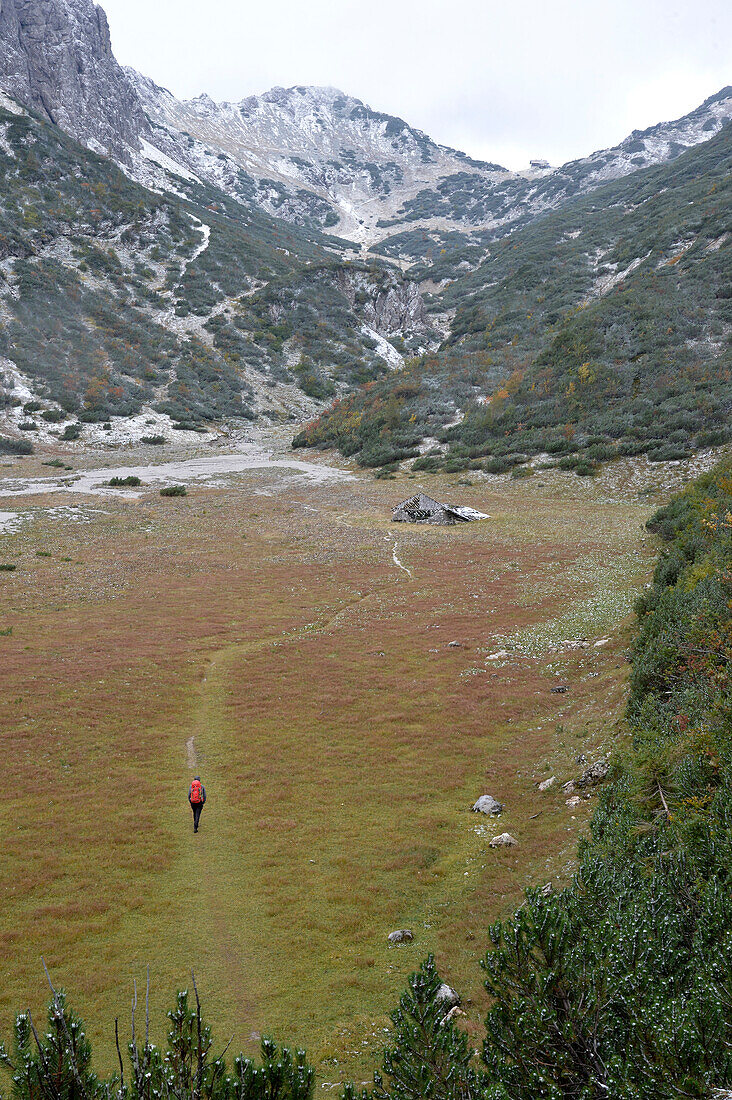 Austria,Styria,ENNSTAL Alps, a man alone carrying a red backpack hikes on a high plateau towards the Admonter mountain hut