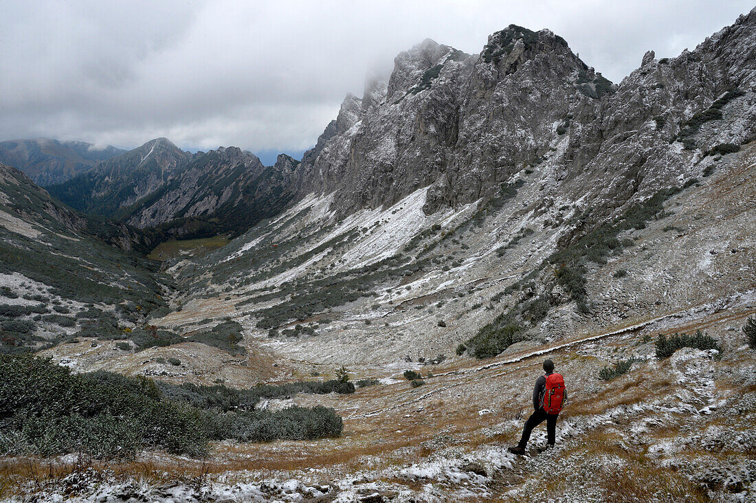 Austria,Styria,ENNSTAL Alps, a man alone carrying a red backpack enjoys the view on a landcsape covered with fresh snow from the Admonter mountain hut