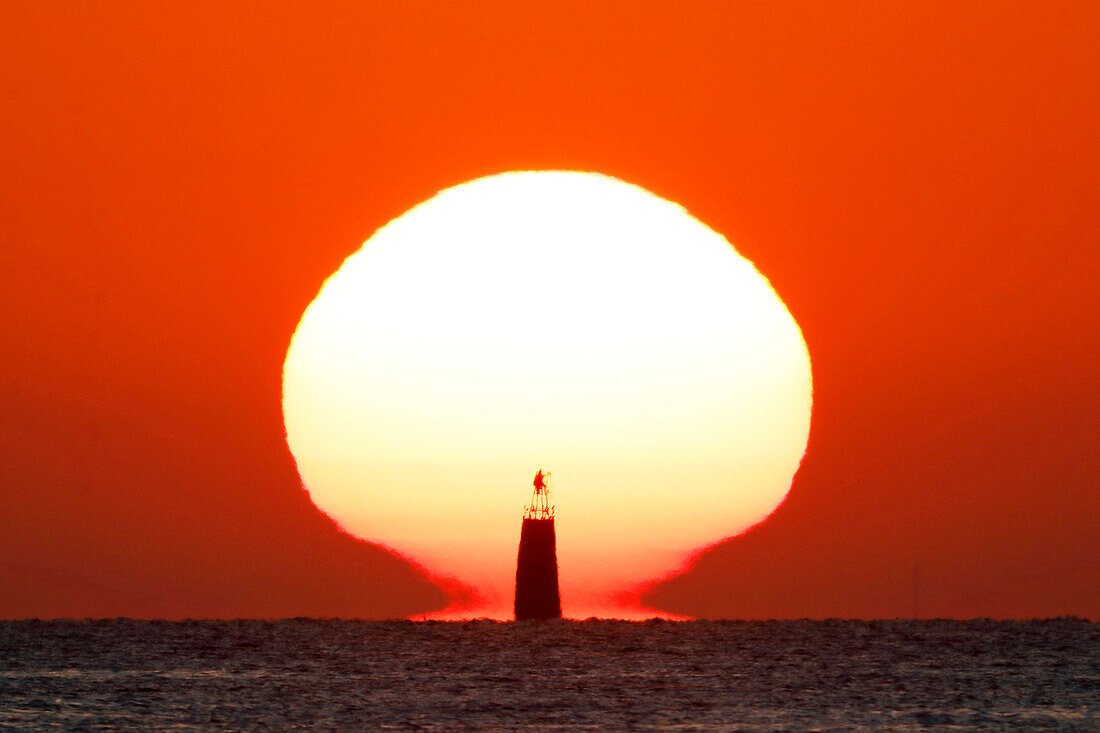 France. Normandy. Department of Manche. Agon-Coutainville. Sunset from Hauteville sur Mer beach in July. In the foreground: the Ronquet lighthouse (beacon light).