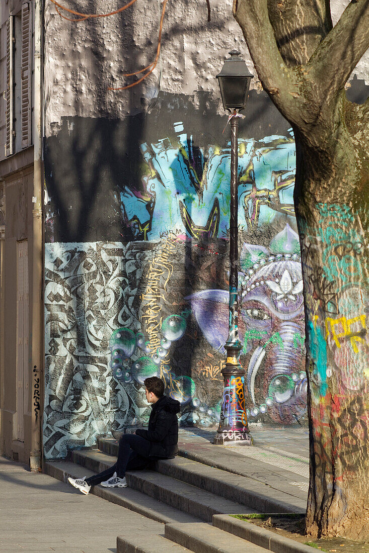 Frankreich,Paris,75,10. ARRT,Rue Jean Poulmarch; zum Canal Saint Martin führend, Jugendlicher sitzt auf der Treppe vor einer mit Graffitis und Malereien bedeckten Wand.