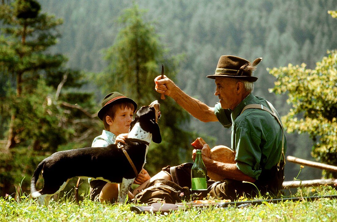Mann, Junge & Hund mit Brotzeit auf einer Wiese in den Bergen