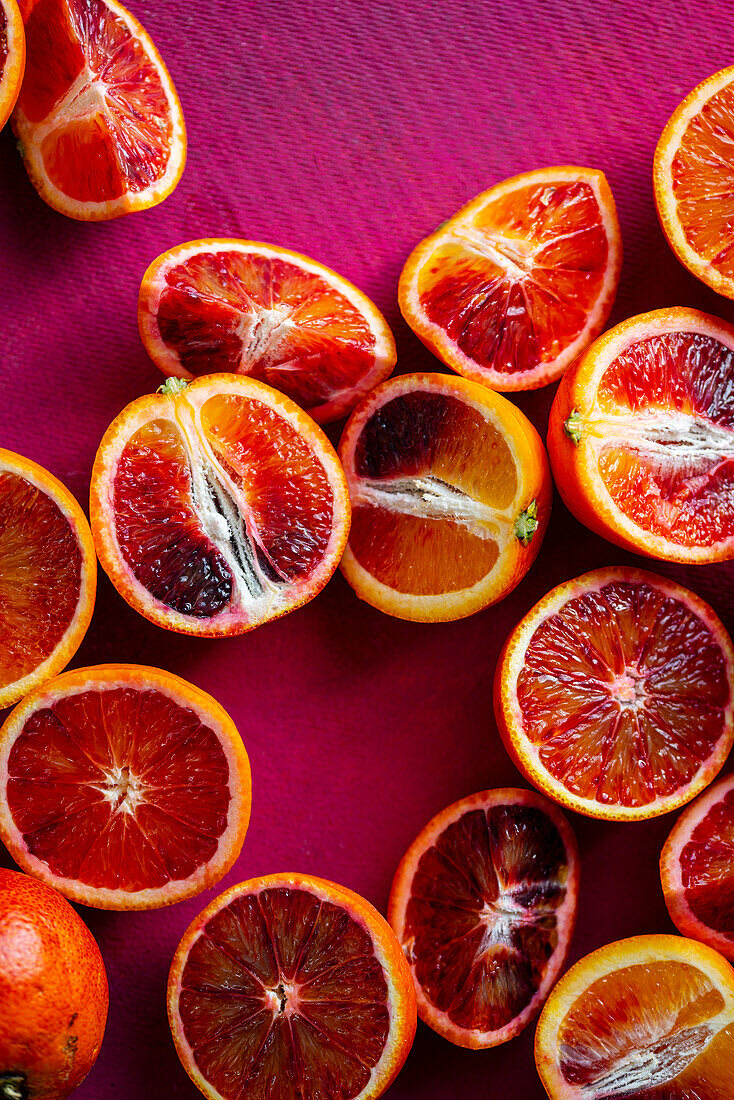 Whole and sliced blood oranges on a pink background