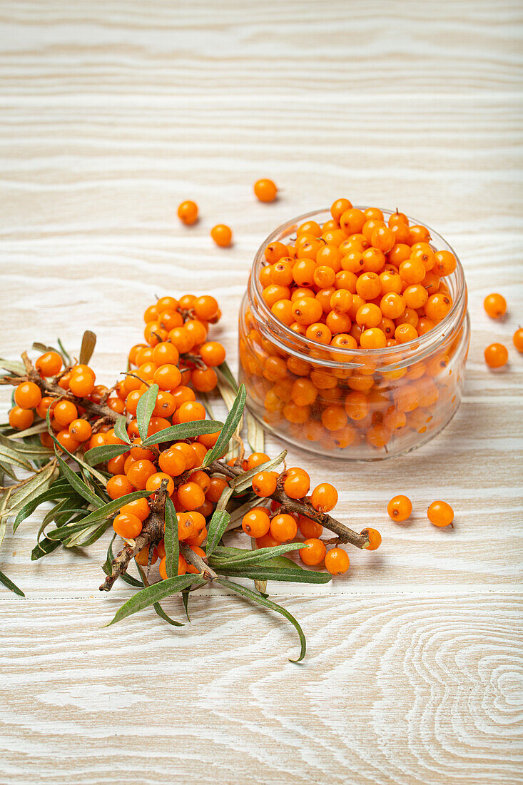 Sea buckthorn berries in a glass next to twigs with leaves