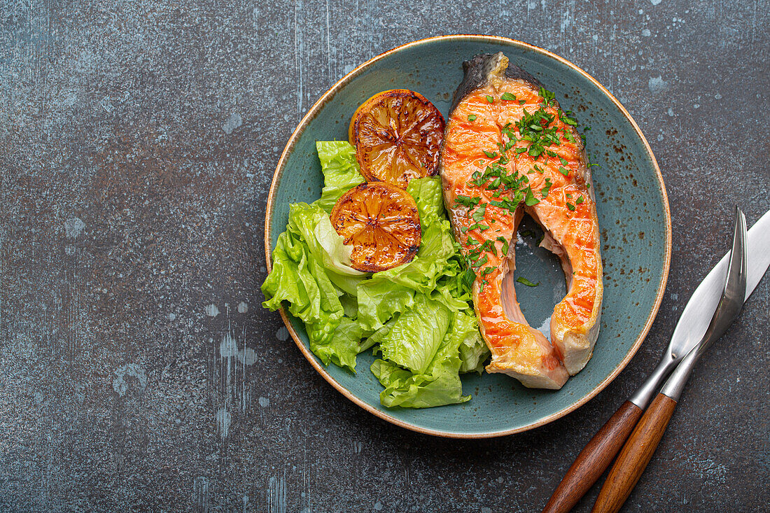 Grilled salmon steak with lemon slices and green salad