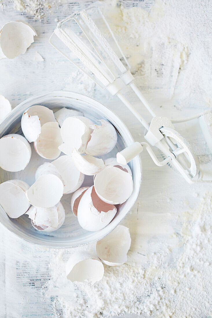 Egg shells and hand whisk on a floured worktop