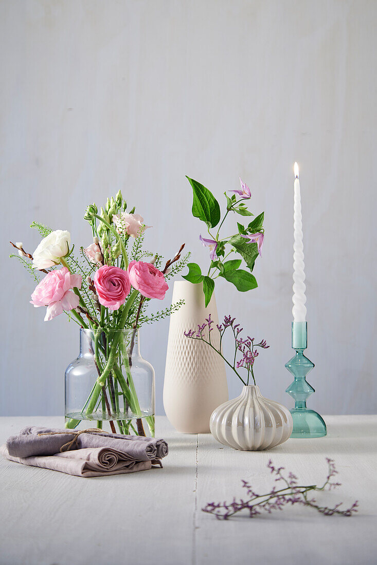 Holztisch mit Blumenarrangement in Glas- und Porzellanvasen mit gedrehter Kerze und Leinenservietten