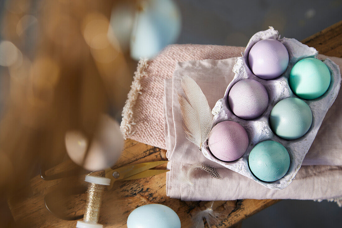 Pastel-coloured Easter eggs in egg carton on pink linen cloth