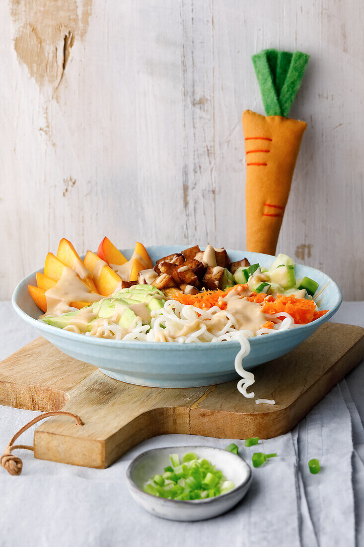 Hand pours dressing over bowl with noodles and fresh vegetables