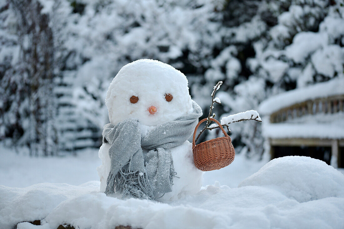 Snowman with grey scarf and basket in snowy garden