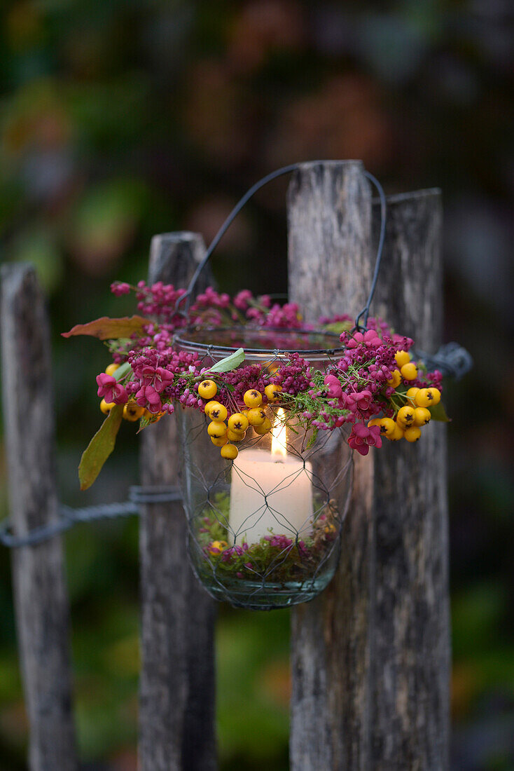 Lantern on a wooden fence with a wreath of heather, coneflower and firethorn berries