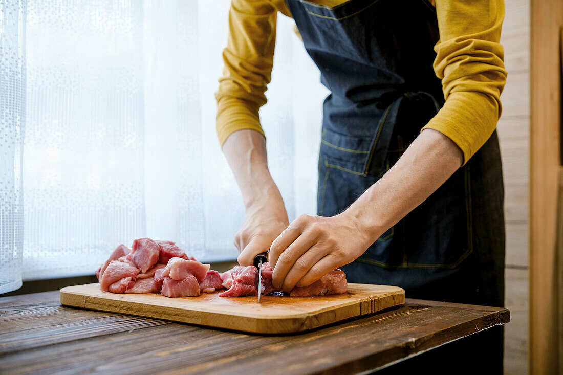 Frau schneidet rohes Schweinefleisch auf Holzbrett