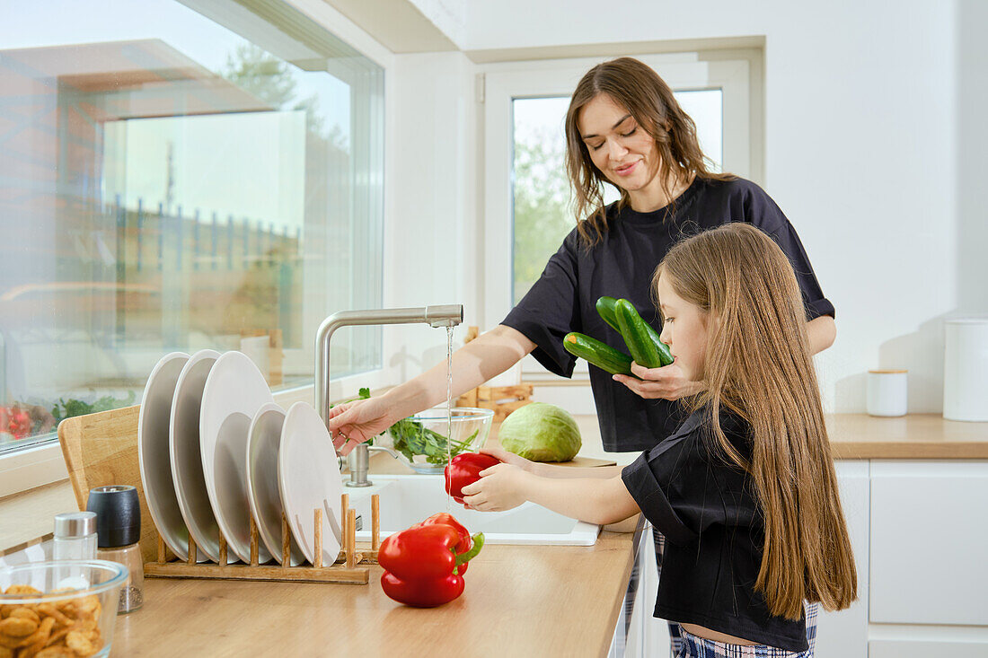 Mädchen und Mutter waschen Paprika und Gurken