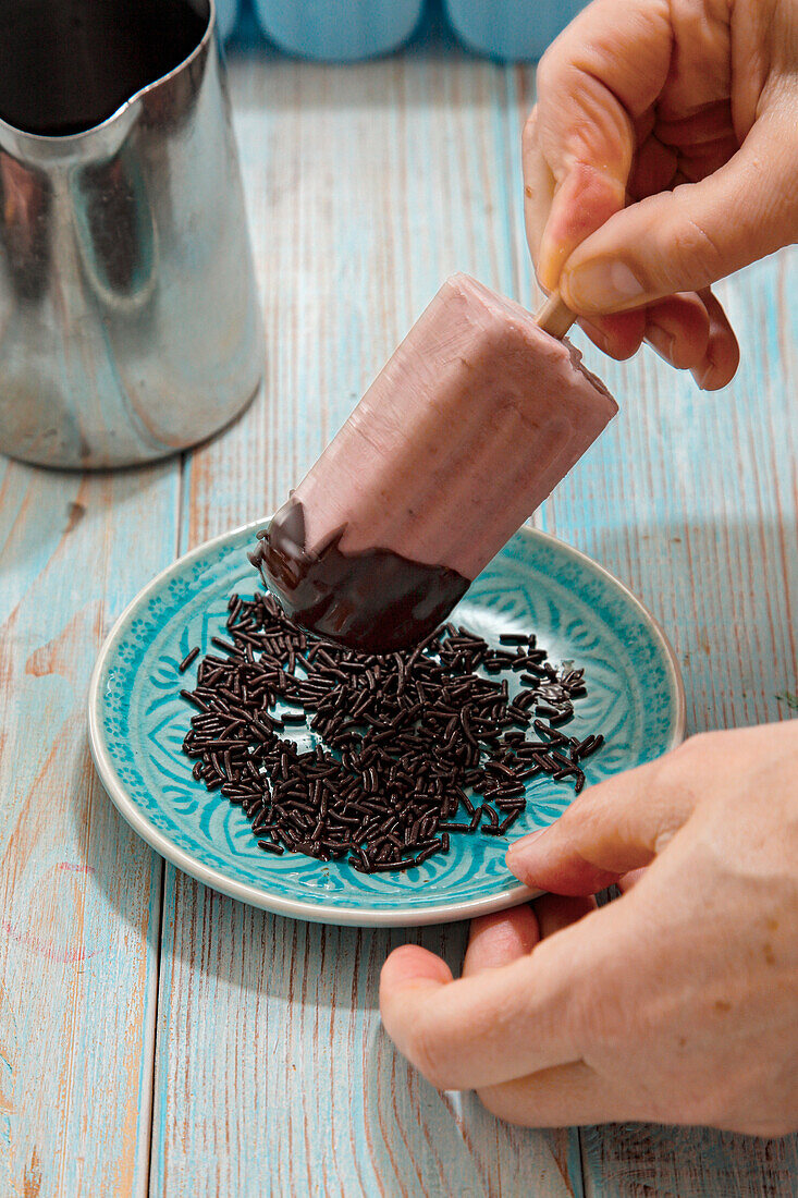 Strawberry and banana ice cream on a stick with chocolate coating and chocolate sprinkles