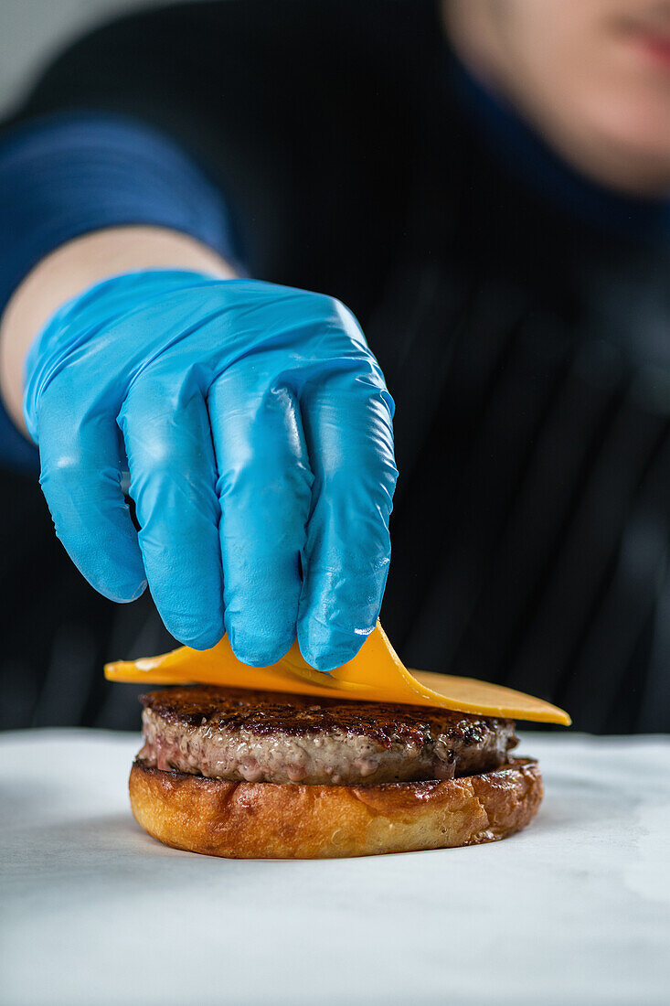 Chef placing slice of cheese onto burger