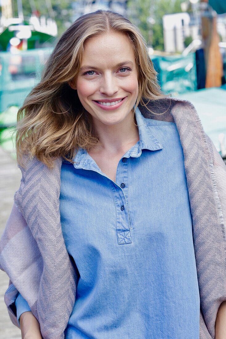 Smiling woman in denim shirt and gray poncho at the harbor