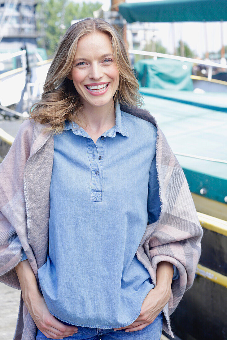 Smiling woman in denim shirt and gray poncho at the harbor