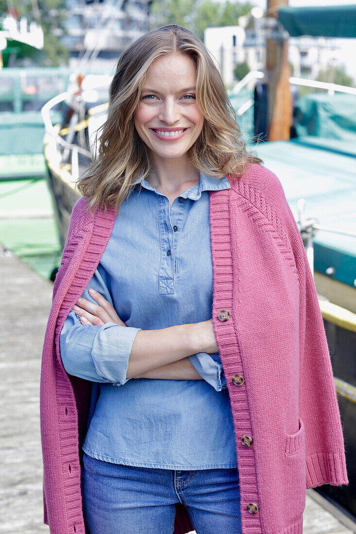 Young woman in jeans outfit and pink cardigan at the harbor