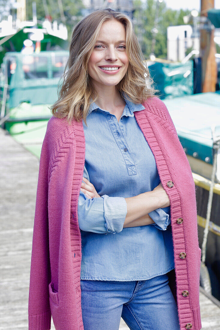 Young woman in jeans outfit and pink cardigan at the harbor