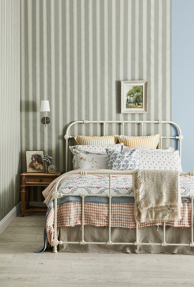 Metallbett mit gemusterten Kissen und Decken und gestreifter Tapete im Schlafzimmer