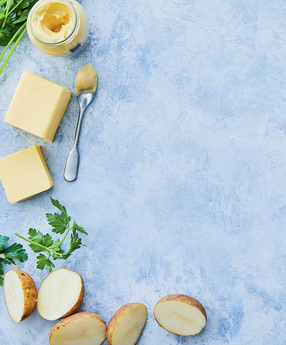 Rohe Kartoffeln, Butter und Senf auf hellblauem Untergrund