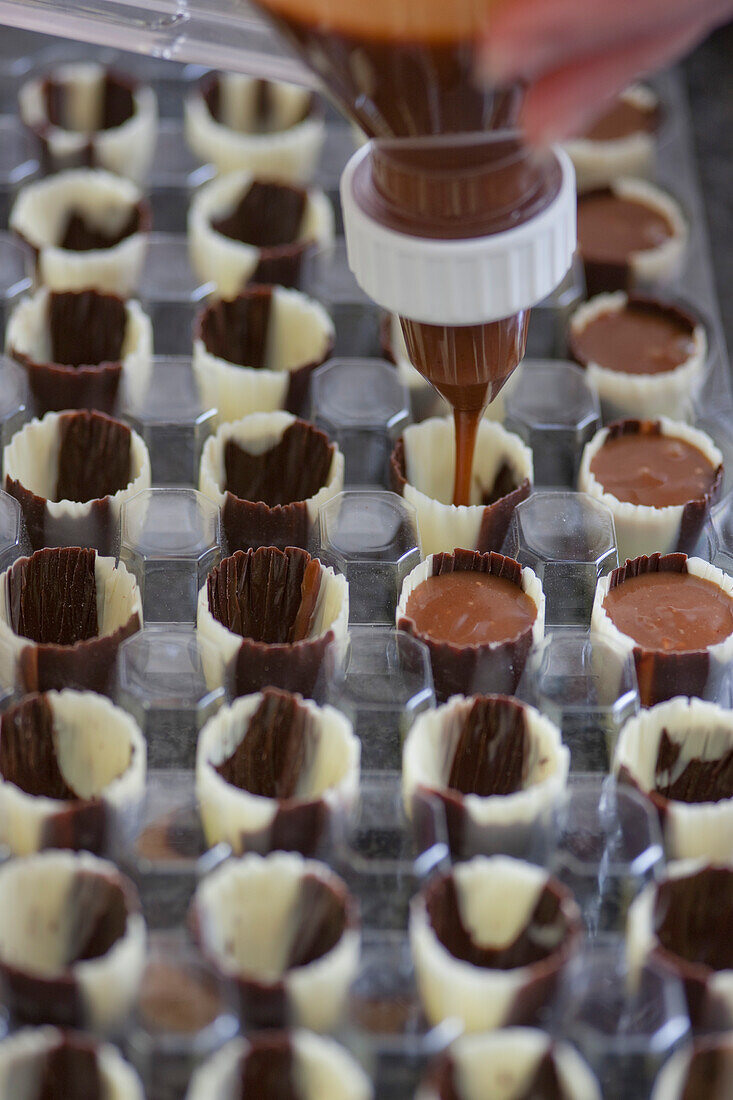 Close up of a chef's hands filling chocolate candy molds