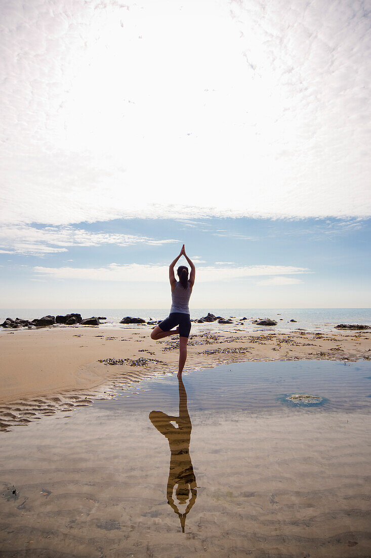 Back view of a woman practicing yoga on a beach