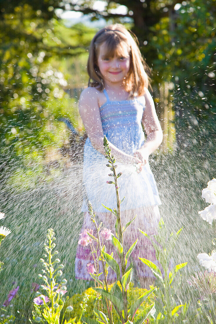 Young Girl Watering Flowers with Garden Hose