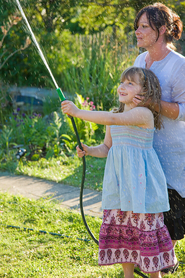 Mutter und Tochter beim Bewässern des Rasens mit einem Gartenschlauch