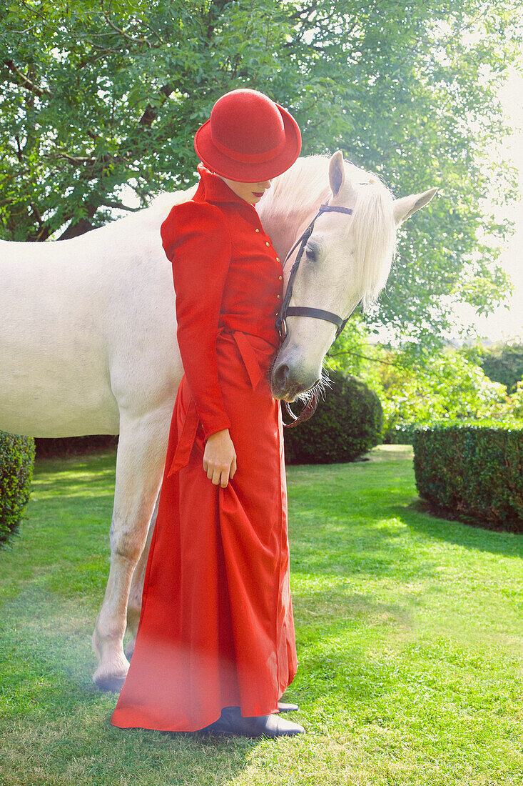 Woman in Red Equestrian Outfit Standing in Garden with Horse