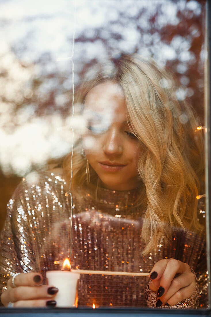 Woman Lighting Candle behind Window pane