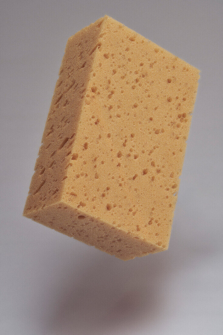 Close detail of brown cleaning sponge floating midair against gray background