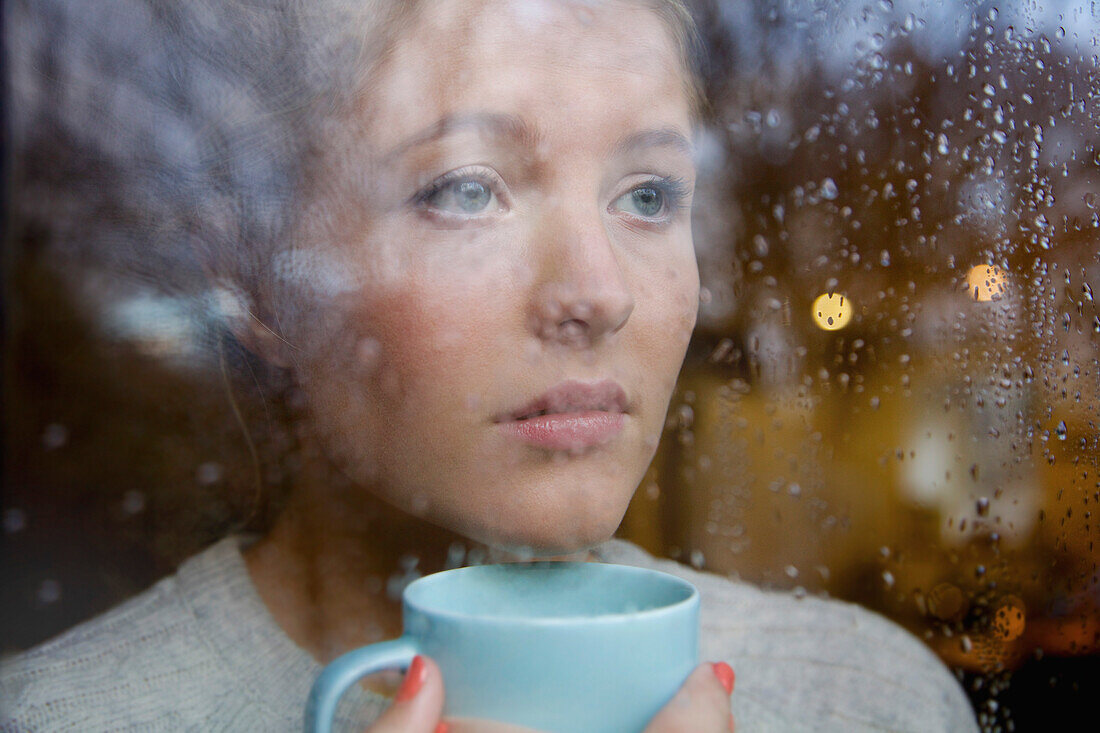 Woman Holding Drinking Cup behind Rainy Window