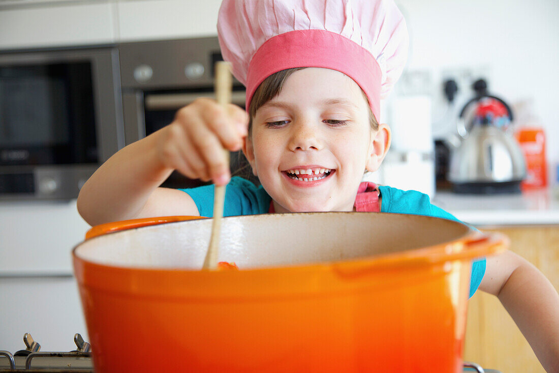 Smiling Girl Wearing Chef's Hat Stirring Casserole