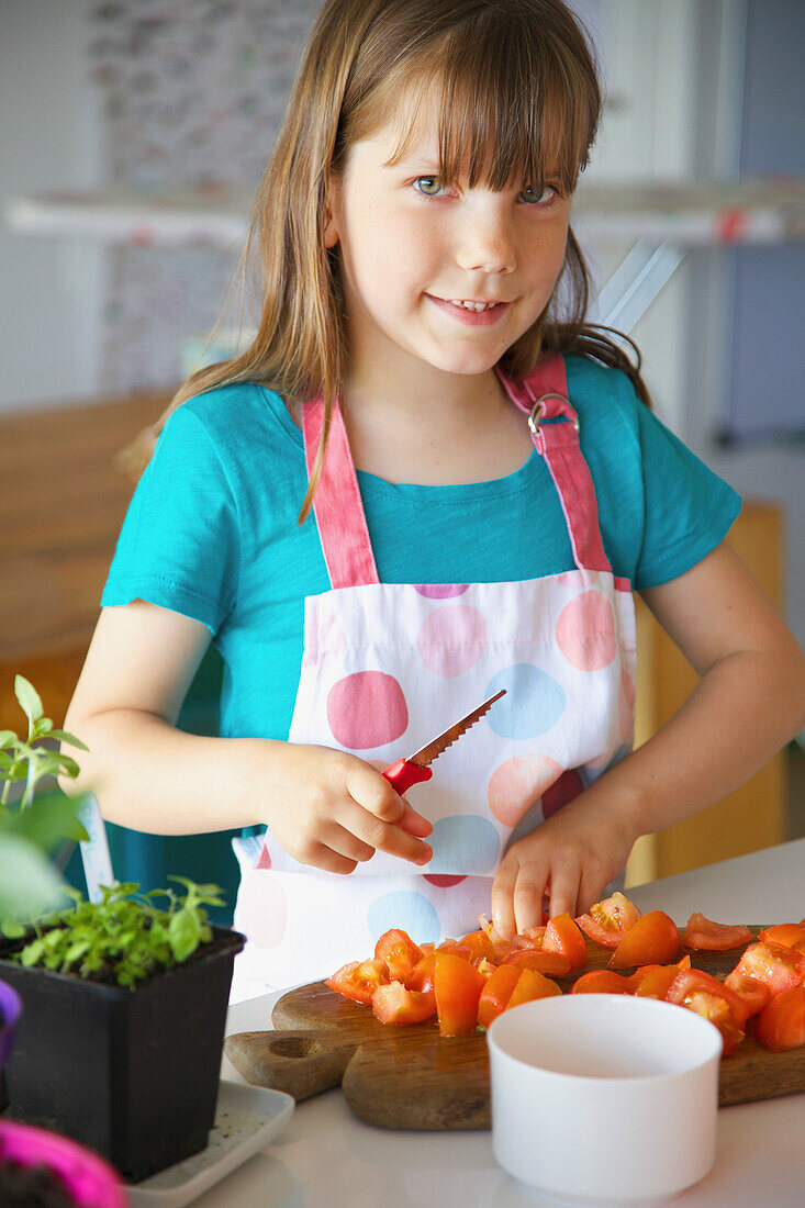 Lächelndes junges Mädchen schneidet Tomaten