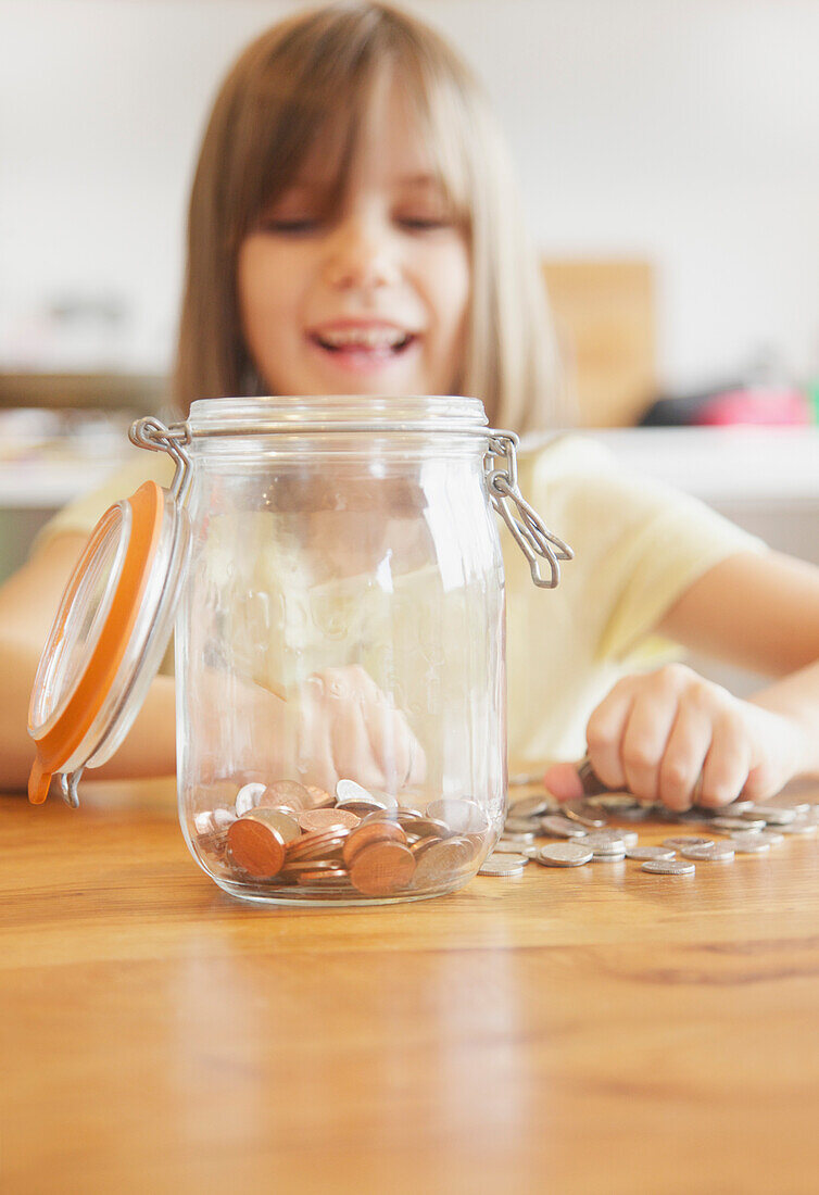 Smiling Young Girl Putting Coins in Jar