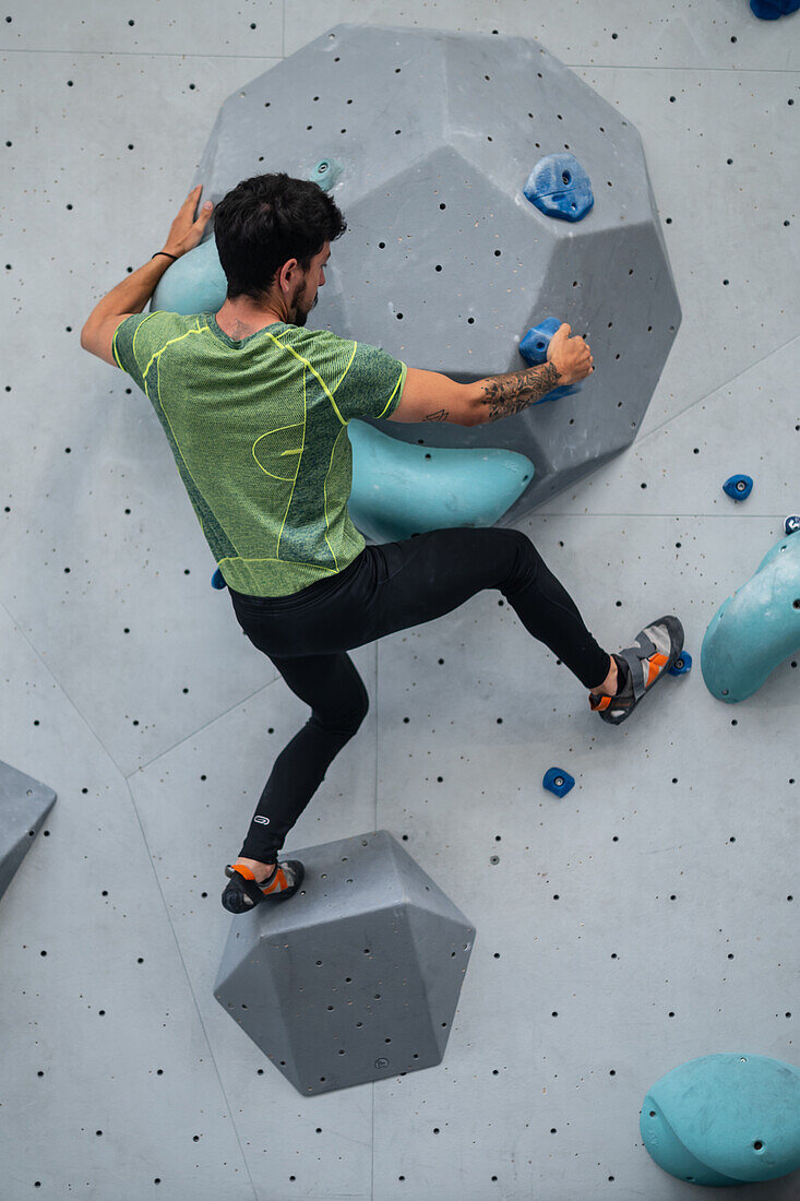 Young man in his twenties climbing on a climbing wall indoors