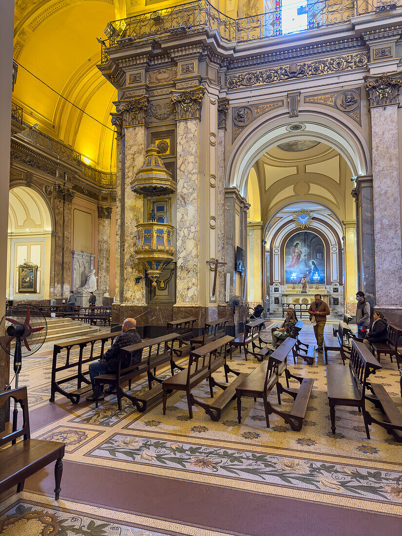 Worshippers, pulpit and side chapel in the Metropolitan Cathedral, Buenos Aires, Argentina. Pulpit was created in 1789-1790 by Spanish sculptor Juan Antonio Gaspar Hernandez in transitional Rococo-Neoclassical style.