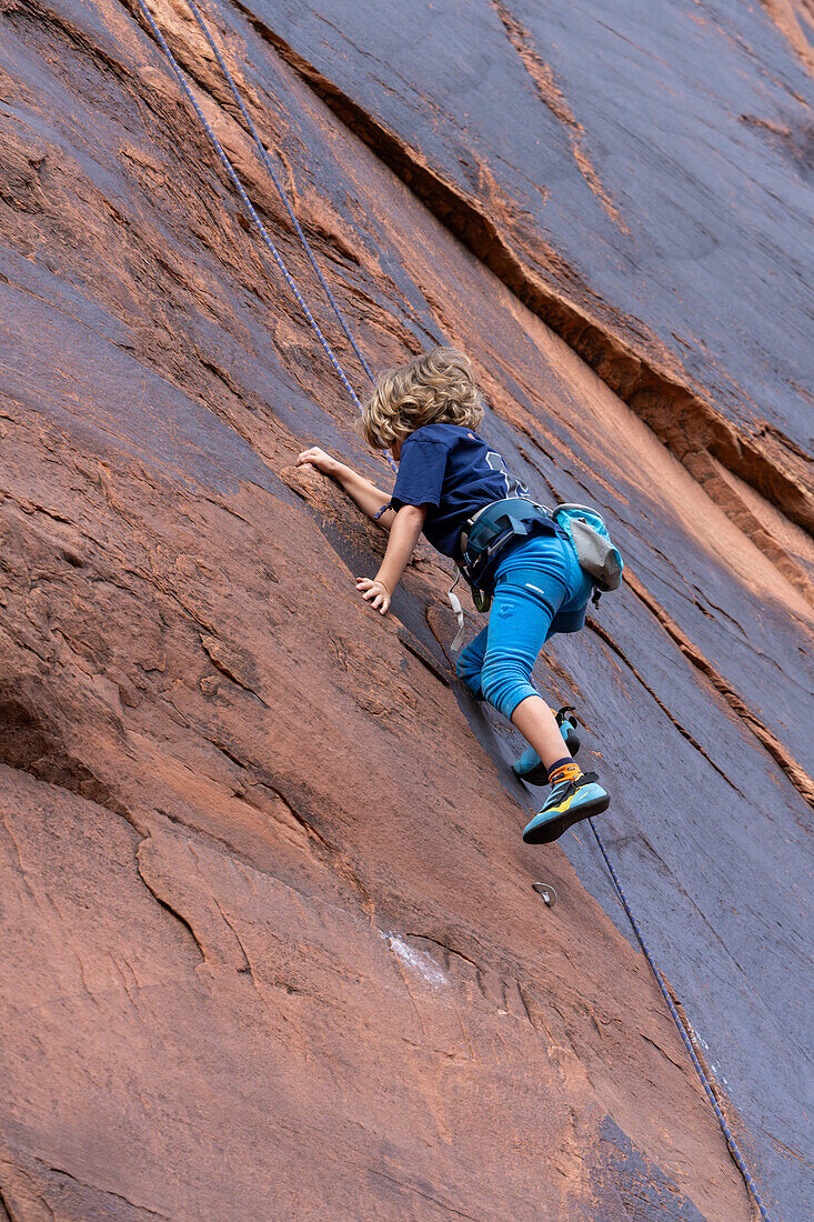 Ein 6-jähriger Junge lernt im Hunter Canyon in der Nähe von Moab, Utah, das Klettern.