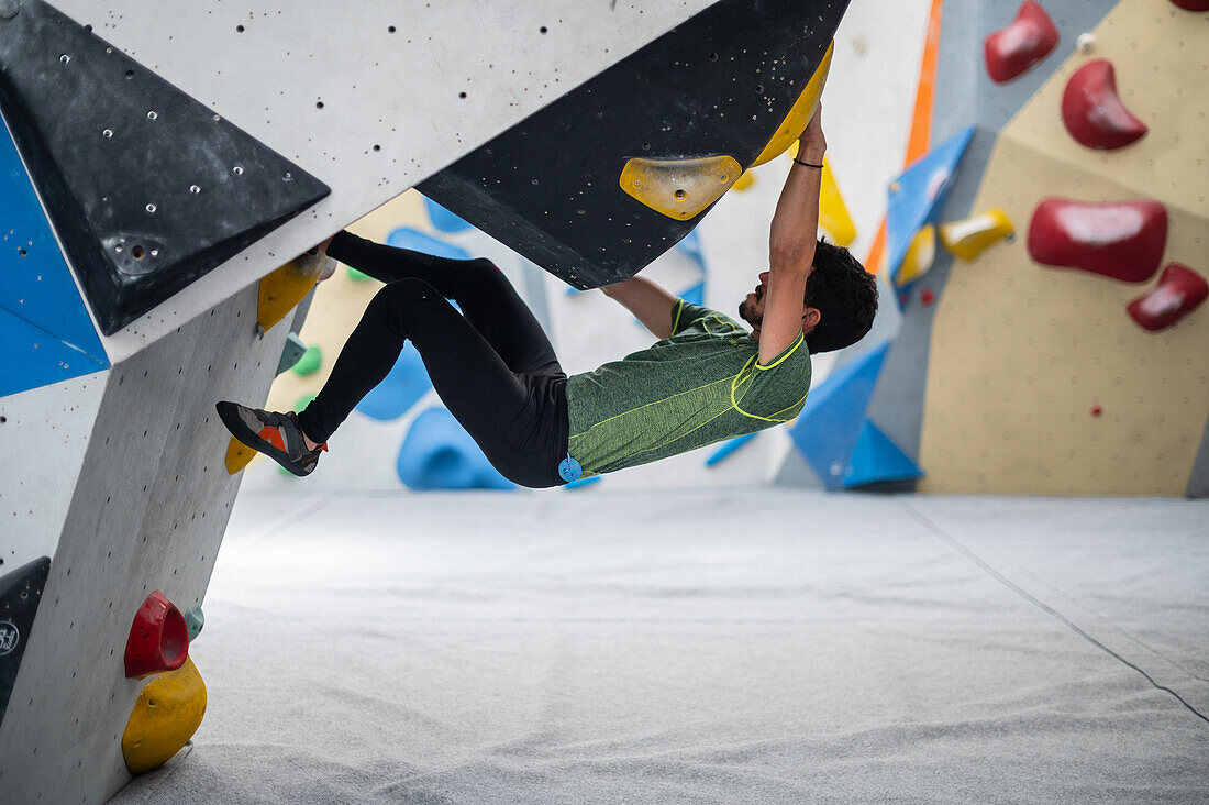 Junger Mann in den Zwanzigern beim Klettern an einer Kletterwand in einer Halle