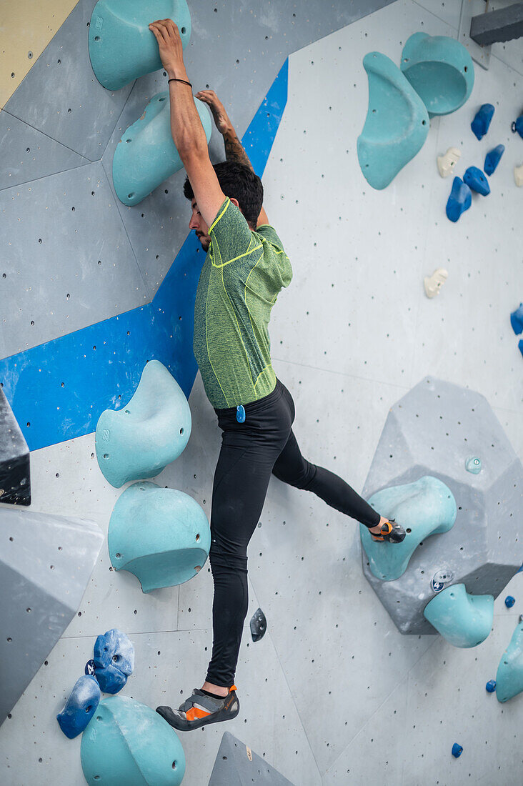 Junger Mann in den Zwanzigern beim Klettern an einer Kletterwand in einer Halle