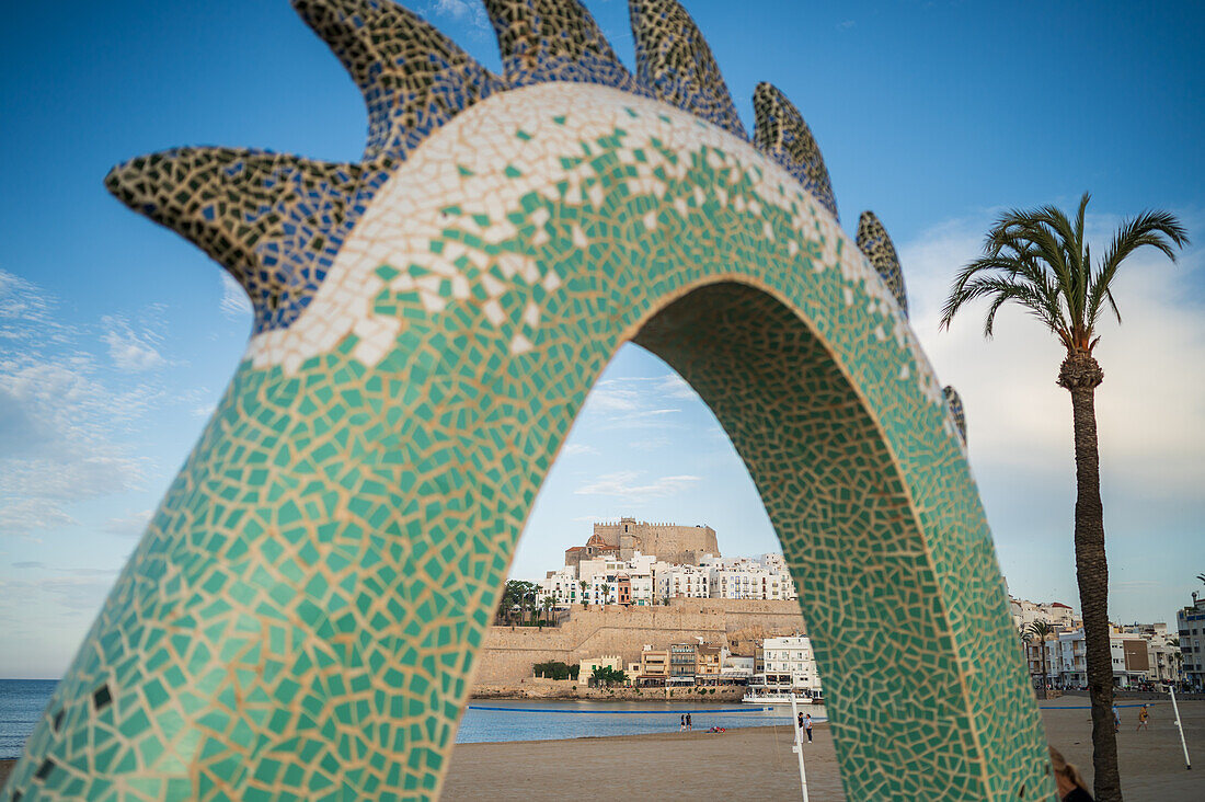 Blick auf die Burg Papa Luna durch die Drachenskulptur an der Strandpromenade in Peñiscola, Castellon, Valencianische Gemeinschaft, Spanien