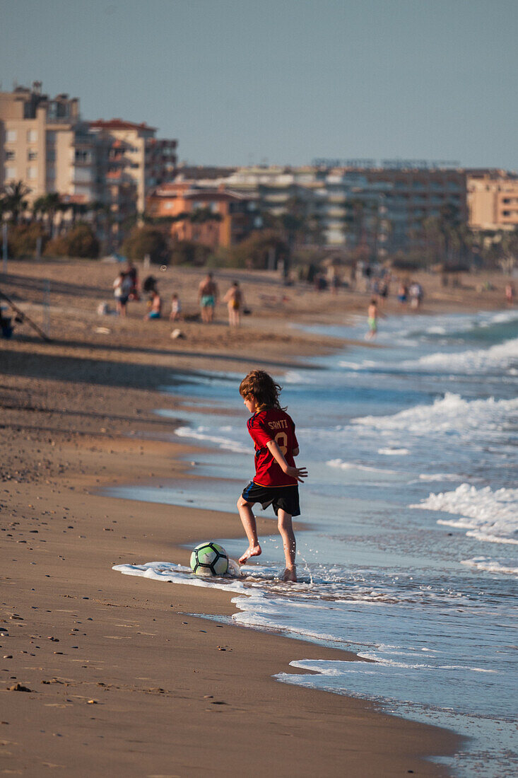 Young boy playing with a ball on Peñiscola Beach, Castellon, Valencian Community, Spain